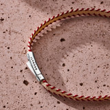 Red and off-white stitched Italian textile bracelet with 925 sterling silver clasp styled on a stone surface