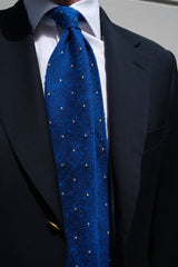 Close-up of the azure blue and white polka dot grenadine shantung silk tie worn with tailored clothing.