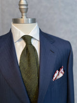 Olive plain grenadine shantung silk tie displayed on a mannequin with a suit and shirt.