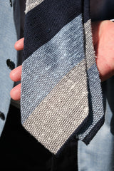 Model holding the navy, white and light blue striped grenadine shantung silk tie toward the camera, showing the textured striped fabric.