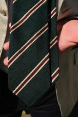 Model holding the forest, beige and burgundy striped silk shantung tie toward the camera, showing the textured striped fabric.